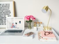 MacBook Air beside gold-colored study lamp and spiral books